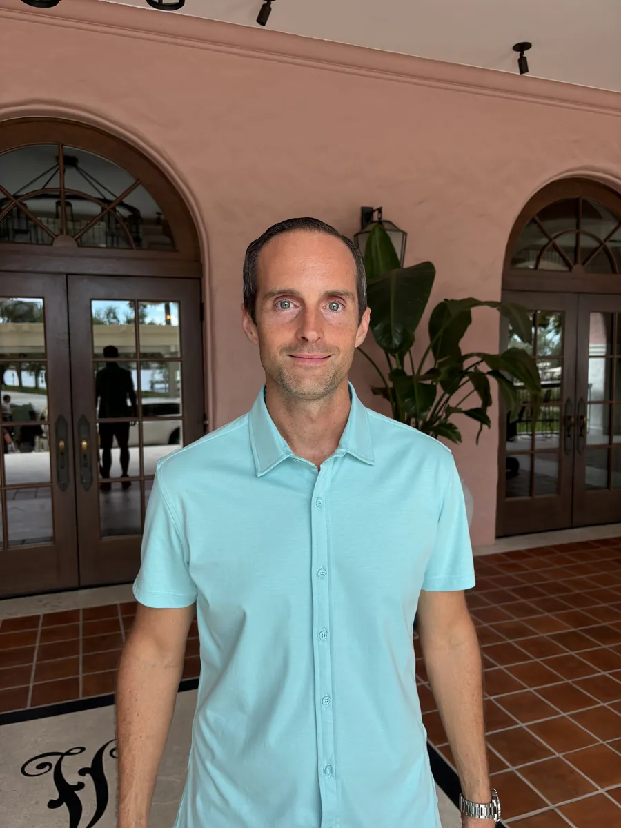 Jerry Banfield smiling in an aqua shirt outside a Spanish-style hotel in St. Petersburg, Florida